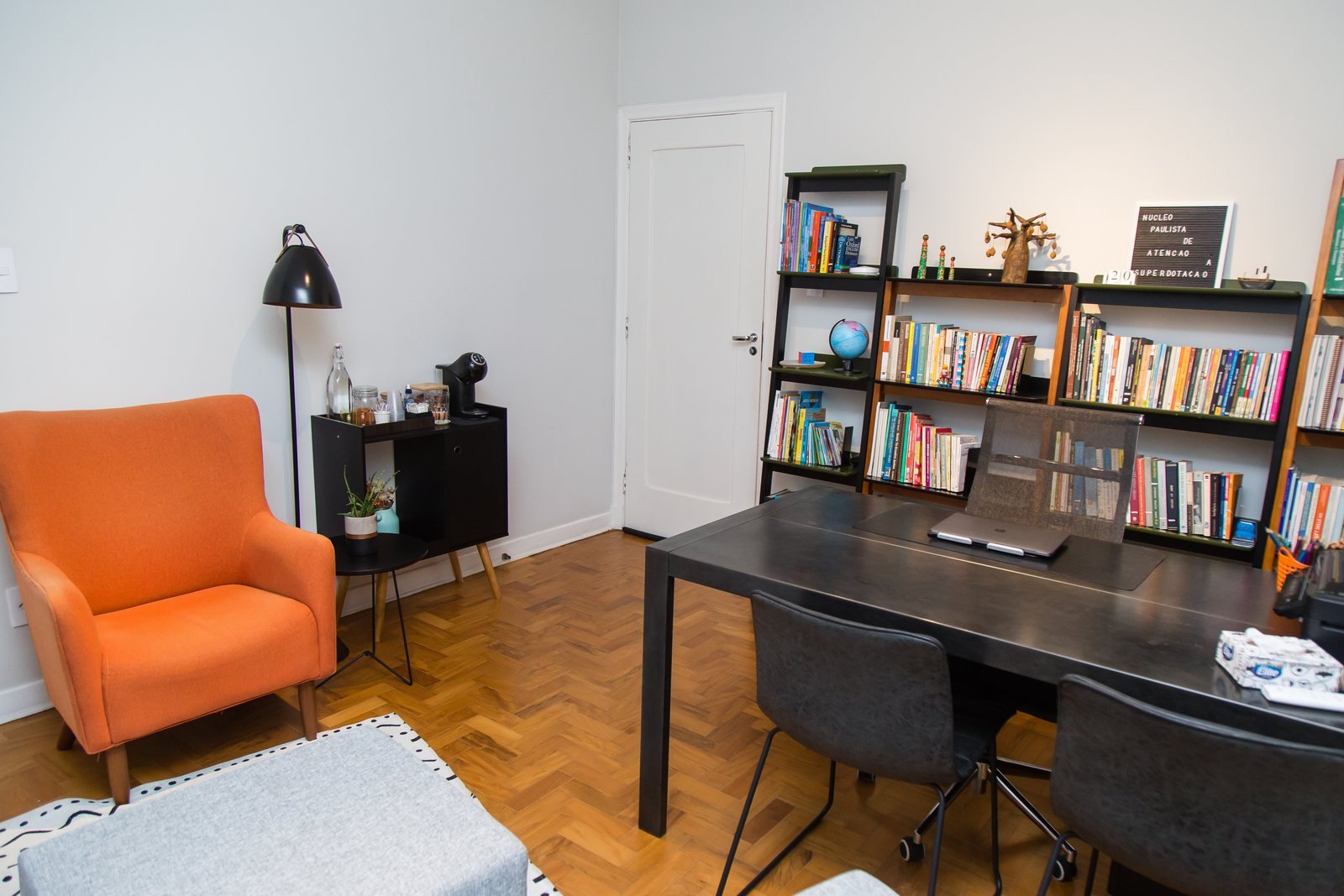 Consultório com poltrona laranja, mesa de trabalho e estantes de livros