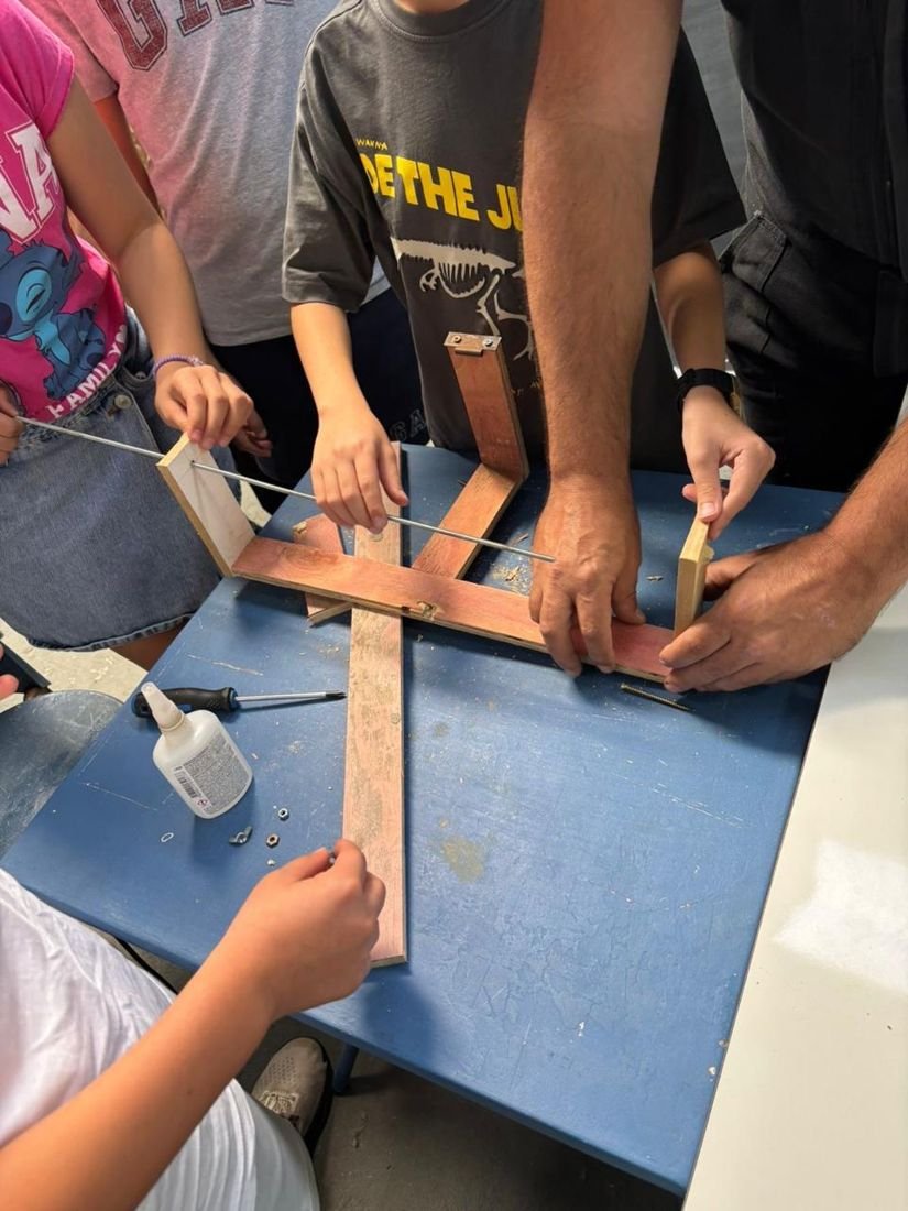 Mãos de crianças e de um tutor montando uma peça de madeira