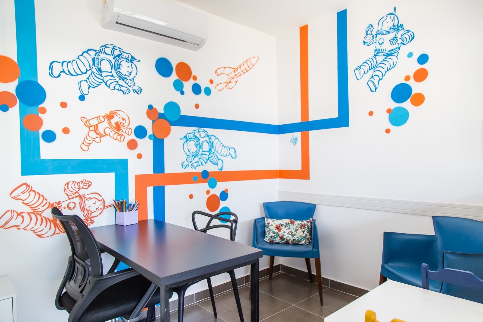 Sala de atendimento com mesa, cadeiras azuis e mural pintado em azul e laranja